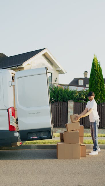 A young woman with long brown hair tied in a ponytail, wearing a white cap and a black sleeveless top, is standing outdoors during a home relocation process. She is holding a clipboard with a pen and